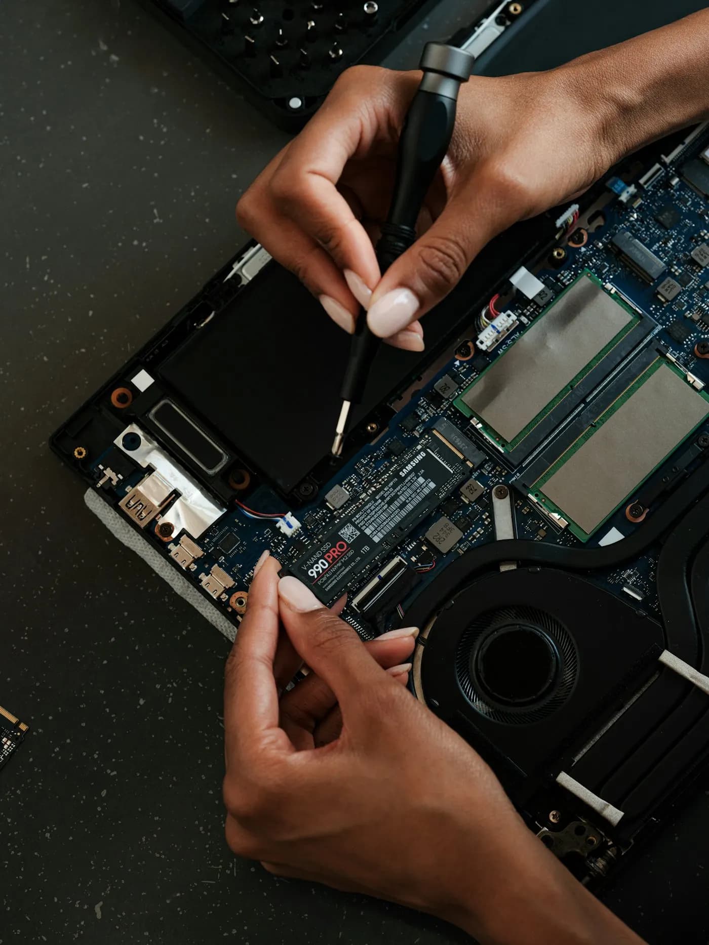 Hands opening the back of a laptop on a repair bench
